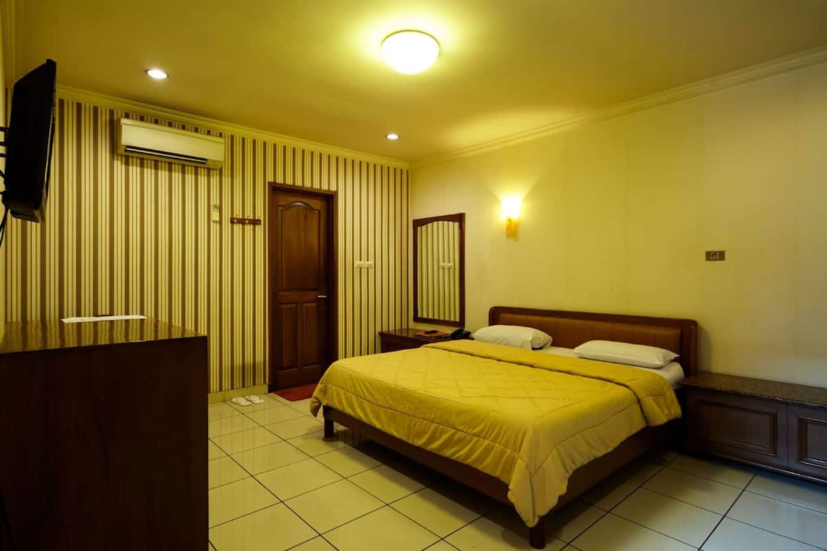A hotel room with a bed, a desk, a mirror, and an air conditioning unit.