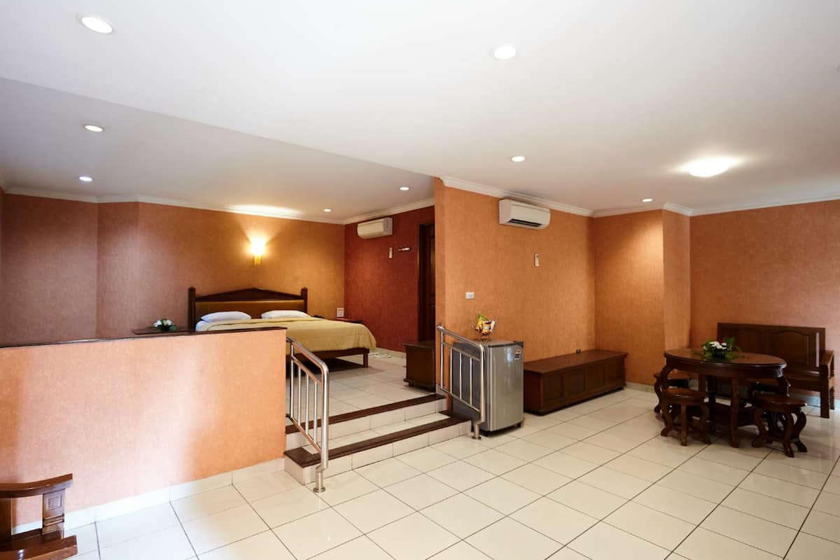 A hotel room with a bed, a desk, a chair, a small refrigerator, and a dining table with chairs.