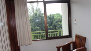 Una habitación con una mesa y sillas de madera, una ventana con vistas a la vegetación y una pared blanca con un interruptor de luz.