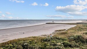 Ein Strand mit breitem Sandufer, wenigen Personen und einem entfernten Steg.