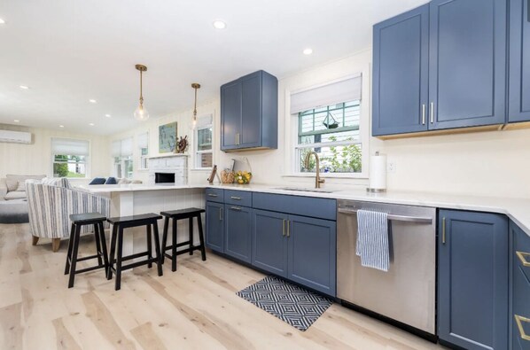 A modern kitchen with dark blue cabinets, a white countertop, and a built-in dishwasher. There are bar stools and a patterned rug on the floor.