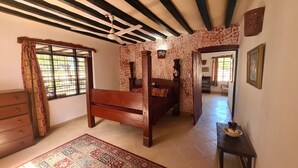 A bedroom with a wooden bed, a dresser, a patterned rug, and a ceiling fan. - Charming 2-Bed Cottage in Bodo, a fishing village (Bodo Village)
