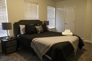 Une chambre à coucher avec un lit, des tables de chevet, des lampes et une porte.