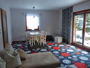 Et værelse med spisebord, stole, sofa og et stort vindue med gardiner.