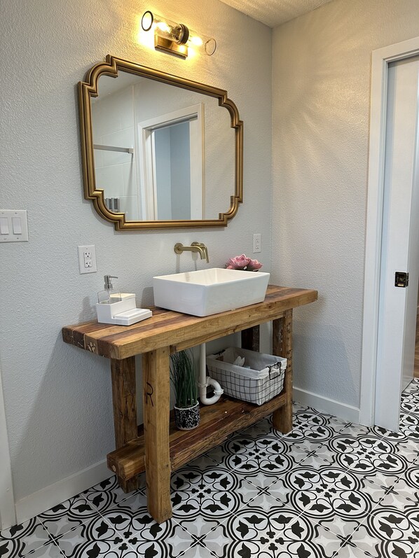 A bathroom with a wooden vanity, white sink, and patterned floor tiles.
