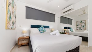 A modern bedroom with a large bed, a nightstand, a mirror, and artwork on the walls. - Stylish 3 BR Apartment in The Heart of Darwin CBD with Pool (Darwin City)