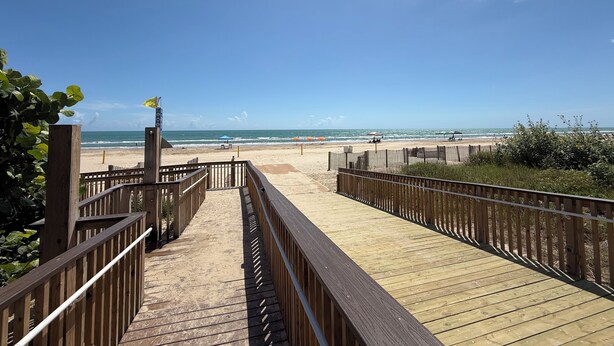 A wooden boardwalk leading to a beach with a clear blue sky.