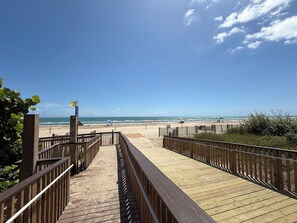 A wooden boardwalk leading to a beach with a clear blue sky.
