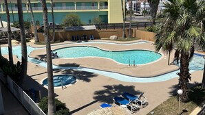 A resort pool area with a circular pool, palm trees, and a building with a red roof in the background.