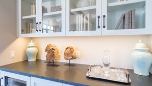 Una cocina con armarios blancos, encimera de granito y elementos decorativos como dos jarrones y una bandeja con vasos.