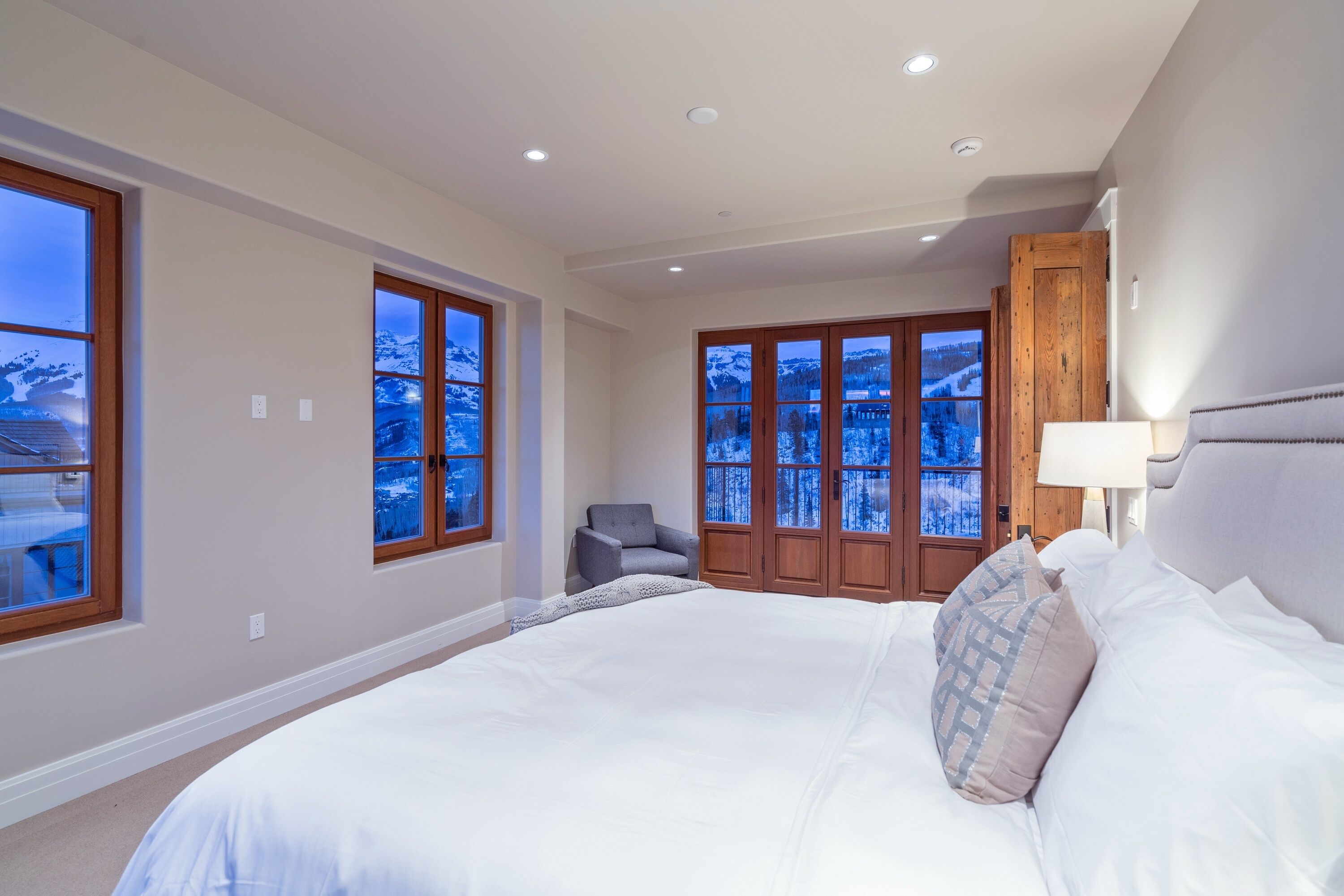 Une chambre avec un grand lit, une chaise, une porte en bois avec des fenêtres et une vue sur un paysage enneigé.