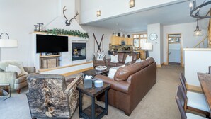 A spacious living area with a fireplace, leather sofas, a television, and a dining area with wooden furniture. - Mountain Village Hideaway 3 Bedroom Townhouse by Alpine Lodging Telluride (Telluride)