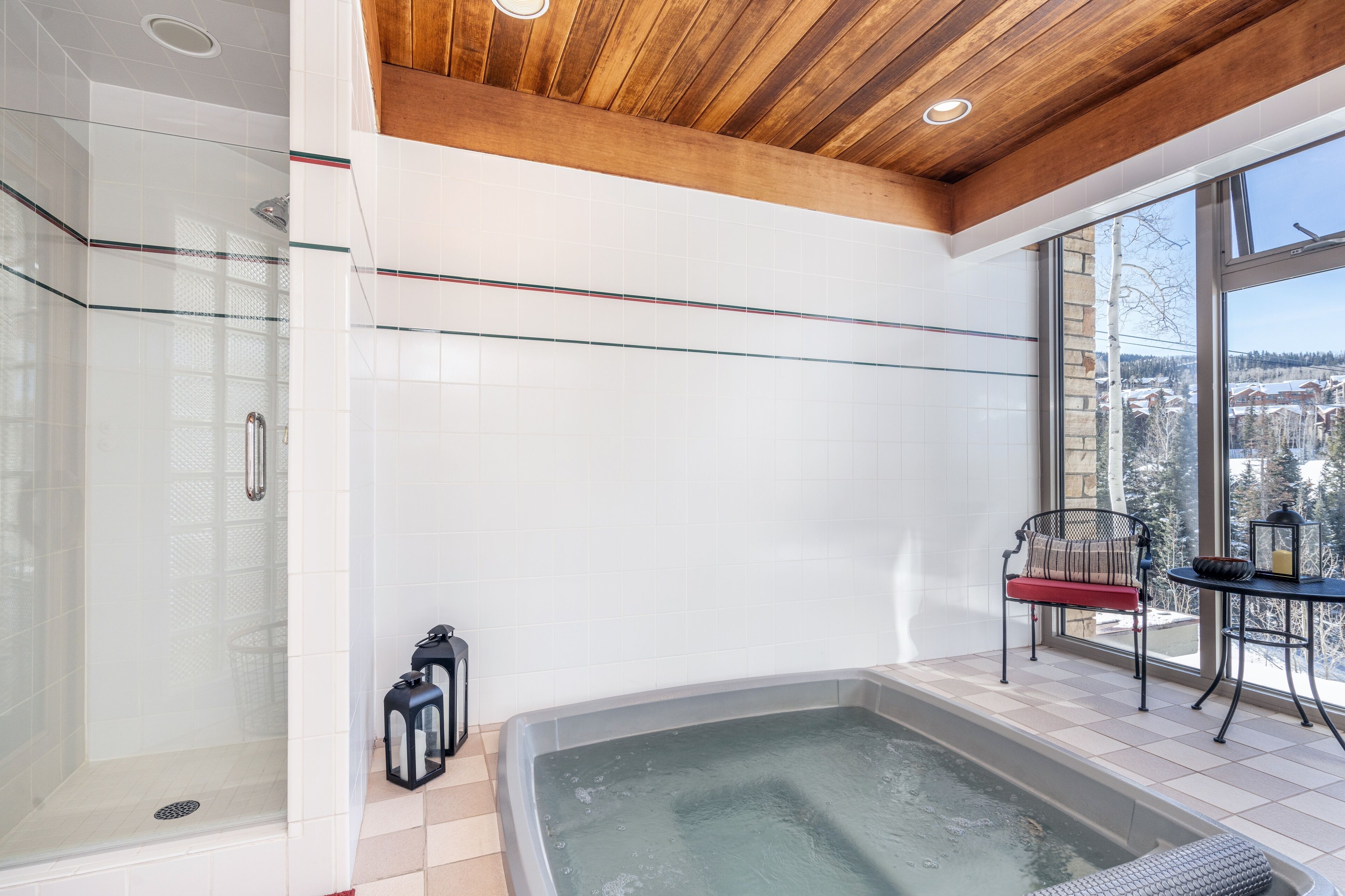 Ein modernes Badezimmer mit Duschkabine aus Glas, einer Badewanne und einer Sitzecke an einem großen Fenster mit Aussicht.