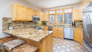 A kitchen with wooden cabinets, granite countertops, a stainless steel refrigerator, and a window providing natural light. - Mountain Village Hideaway 3 Bedroom Townhouse by Alpine Lodging Telluride (Telluride)