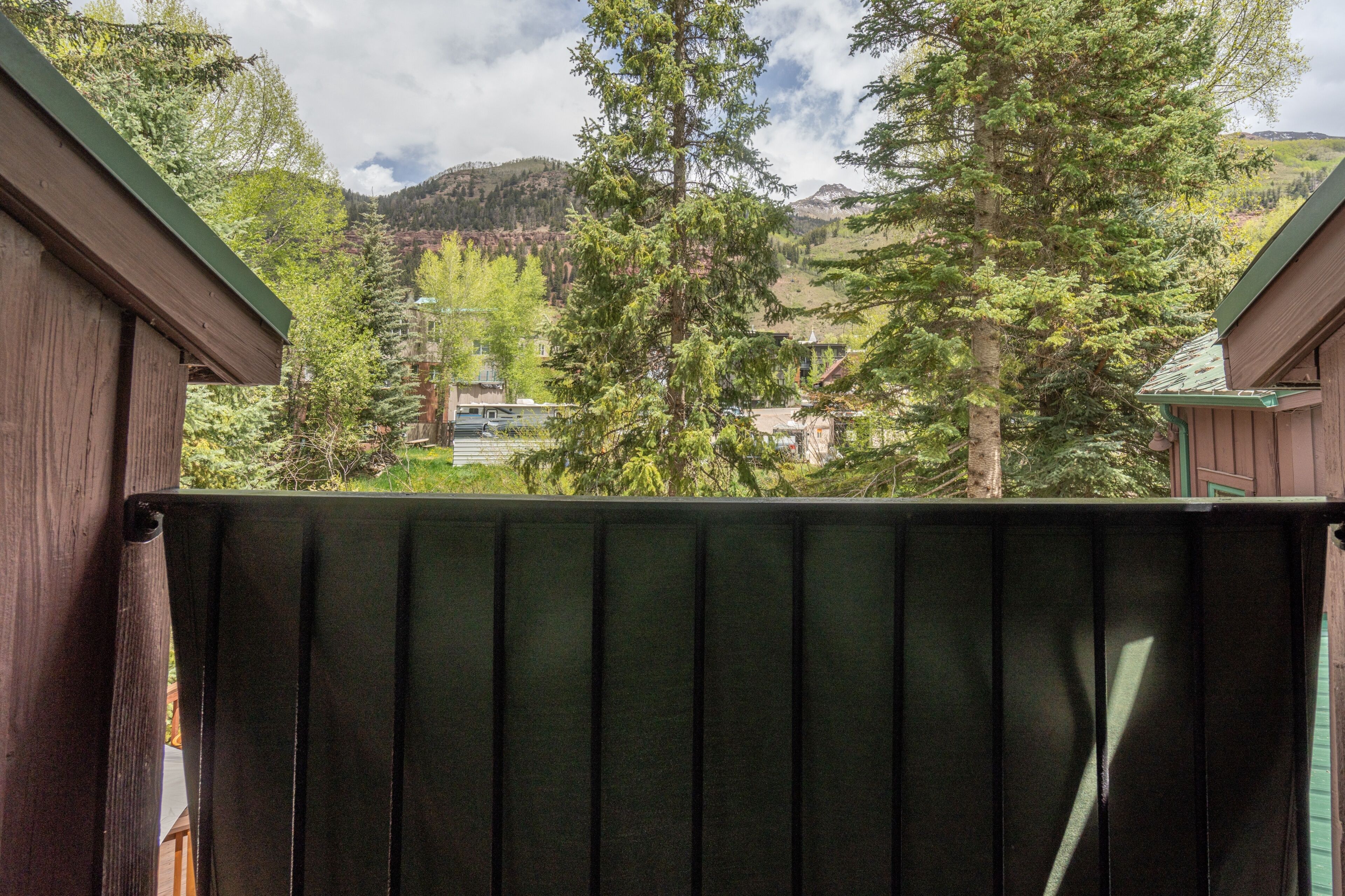 Una terraza de madera con vista a un paisaje montañoso y una casa al fondo.