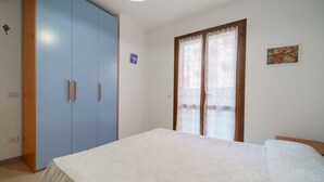 A bedroom with a bed, a wardrobe, and a window with lace curtains. - APPARTAMENTI BILO SOFI - BILO SOFI CON GIARDINO (Campo nell'Elba)