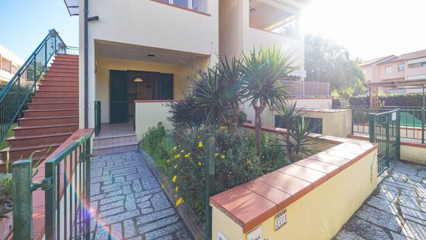 A multi-story building with a staircase leading to the entrance, a small garden with yellow flowers, and a gated area. - APPARTAMENTI BILO SOFI - BILO SOFI CON GIARDINO (Campo nell'Elba)