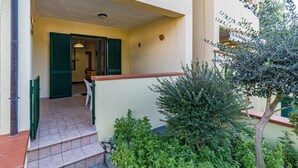A building entrance with a tiled porch, green shutters, and a small garden with a tree and shrubs. - APPARTAMENTI BILO SOFI - BILO SOFI CON GIARDINO (Campo nell'Elba)