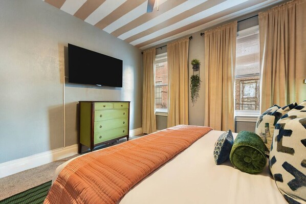 A bedroom with a bed, a green dresser, a flat-screen TV, and a window with curtains.