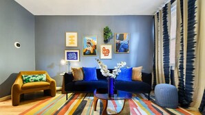 Ein modernes Wohnzimmer mit einem blauen Sofa, einem farbenfrohen Streifen Teppich und Kunstwerken an der Wand.