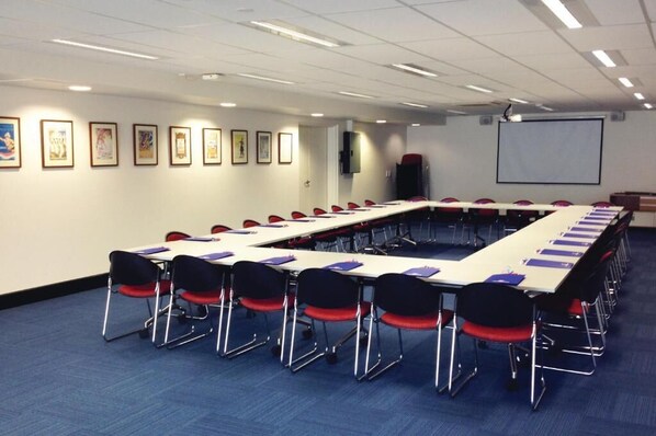 A conference room with a long table, red chairs, and framed pictures on the wall.