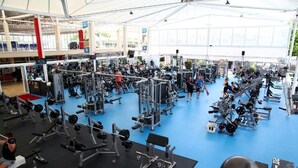 A gym with various exercise equipment, a blue floor, and a covered area with natural light. - Gold Coast Performance Centre - Hostel (Runaway Bay)