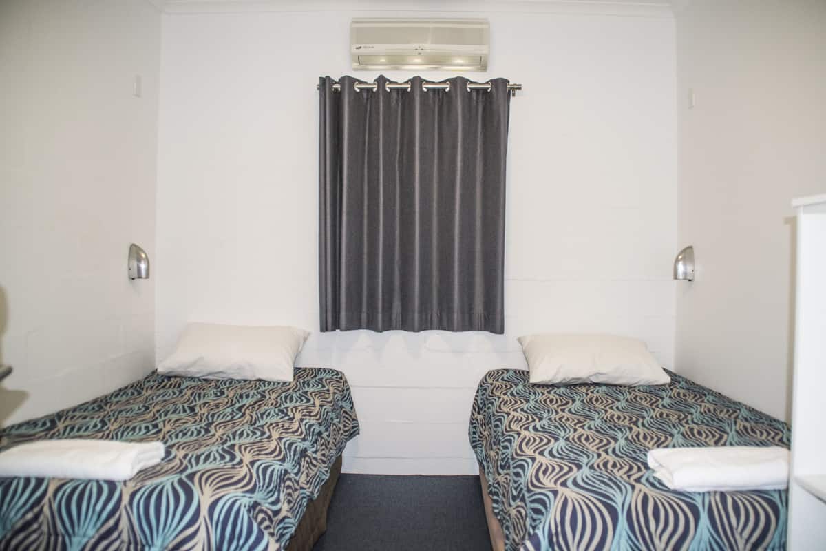 A room with two single beds, a window with a curtain, and a wall-mounted air conditioner.