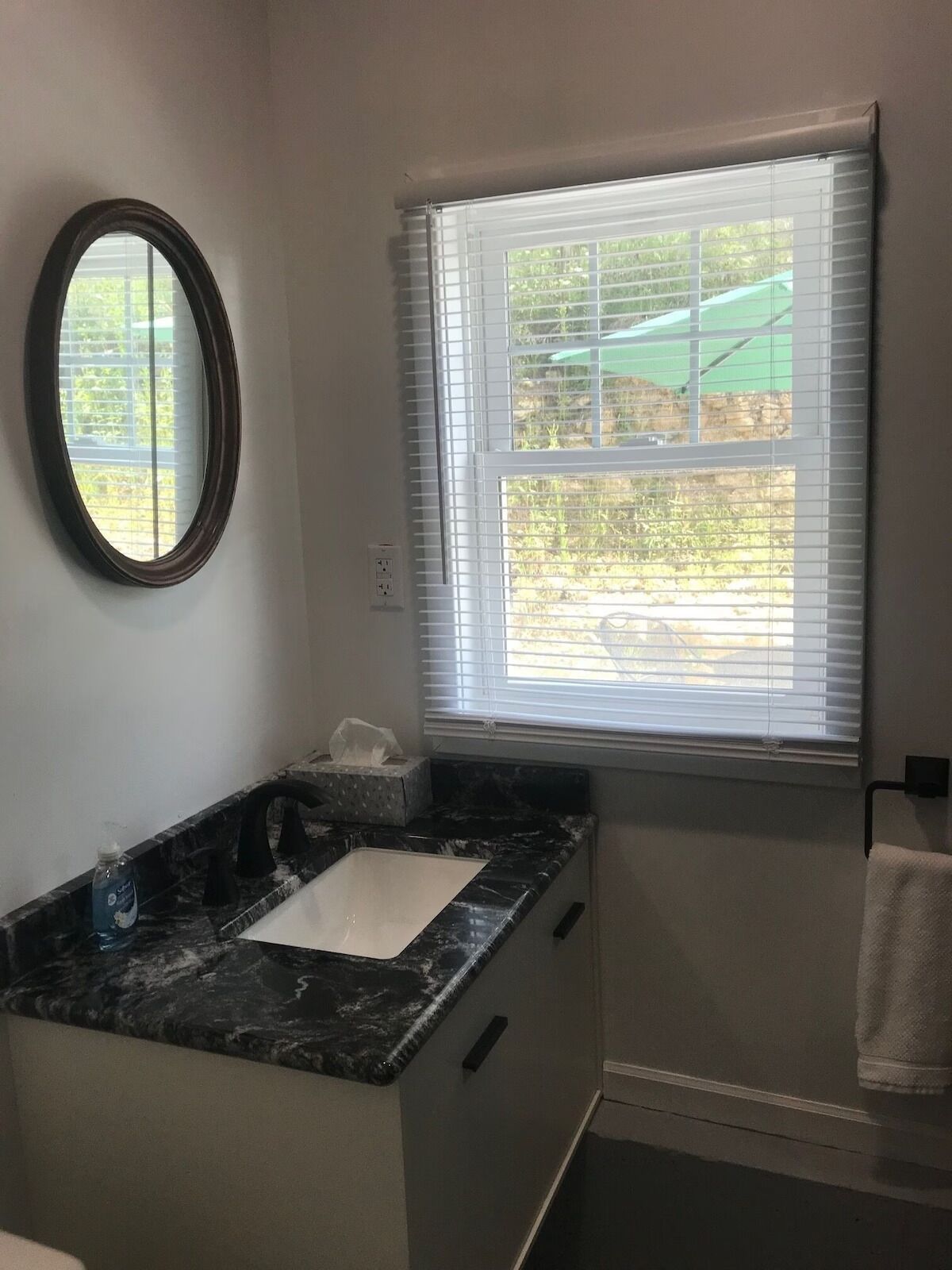 A bathroom with a marble sink, a mirror, a window with blinds, and a towel hanging on a rack.