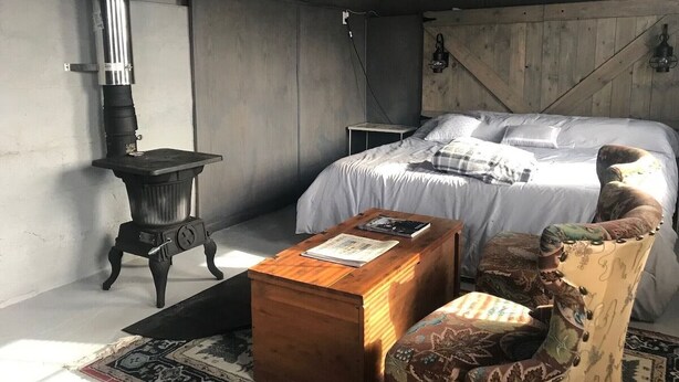 Een slaapkamer met een bed, een houten kist, een stoel, een klein tafeltje en een houtkachel.