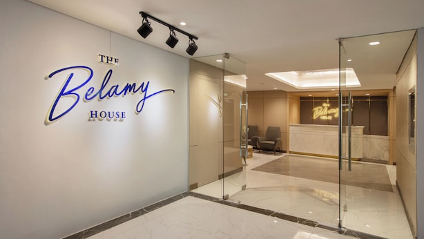 A modern hotel lobby with a glass partition, a reception desk, and a wall sign reading "The Belamy House". - The Belamy House Managed by HII  (Makati)