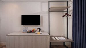 A modern hotel room with a flat-screen TV mounted on the wall, a wooden cabinet with a coffee maker, and a small table with a towel and a handwritten note. - The Belamy House Managed by HII  (Makati)