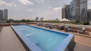 A rooftop swimming pool with lounge chairs and umbrellas, surrounded by high-rise buildings. - The Belamy House Managed by HII  (Makati)