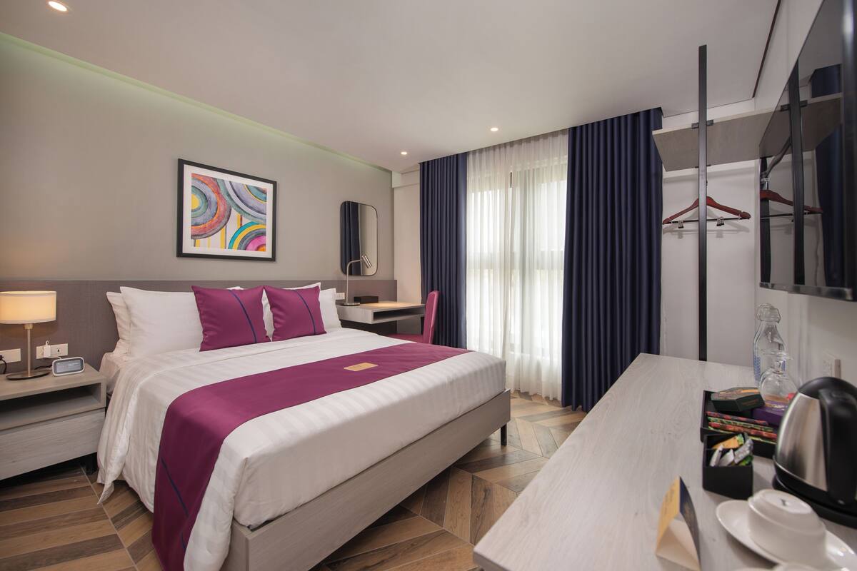 Una habitación de hotel moderna con una cama grande, un escritorio, una silla, un espejo y un armario.