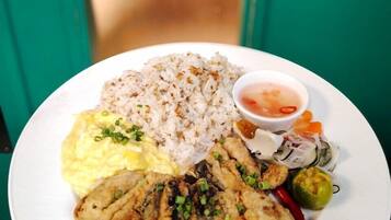 A plate of food with rice, scrambled eggs, grilled meat, and a side of vegetables and sauce.