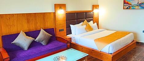 A room with a wooden ceiling, a bed with a headboard, a sofa, a small table, and a painting on the wall.