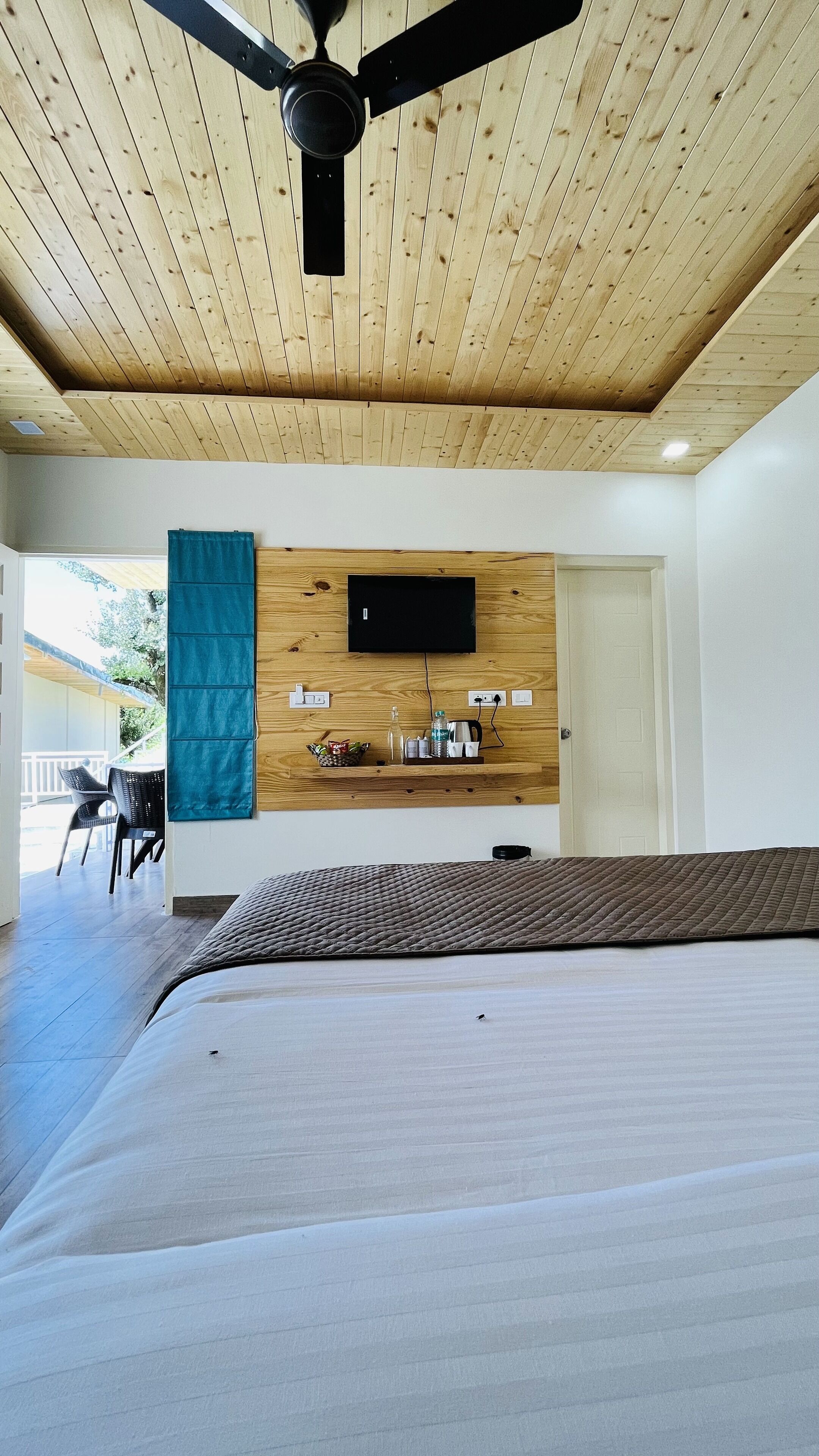 Un dormitorio con cama, ventilador de techo, televisor montado y pared de madera con estante.
