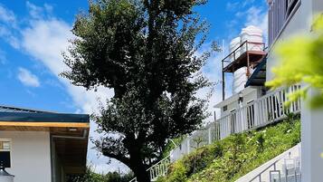Ein Terrassenbereich im Freien mit weißem Zaun, einem großen Baum und einer Treppe, die zu einem Gebäude führt.