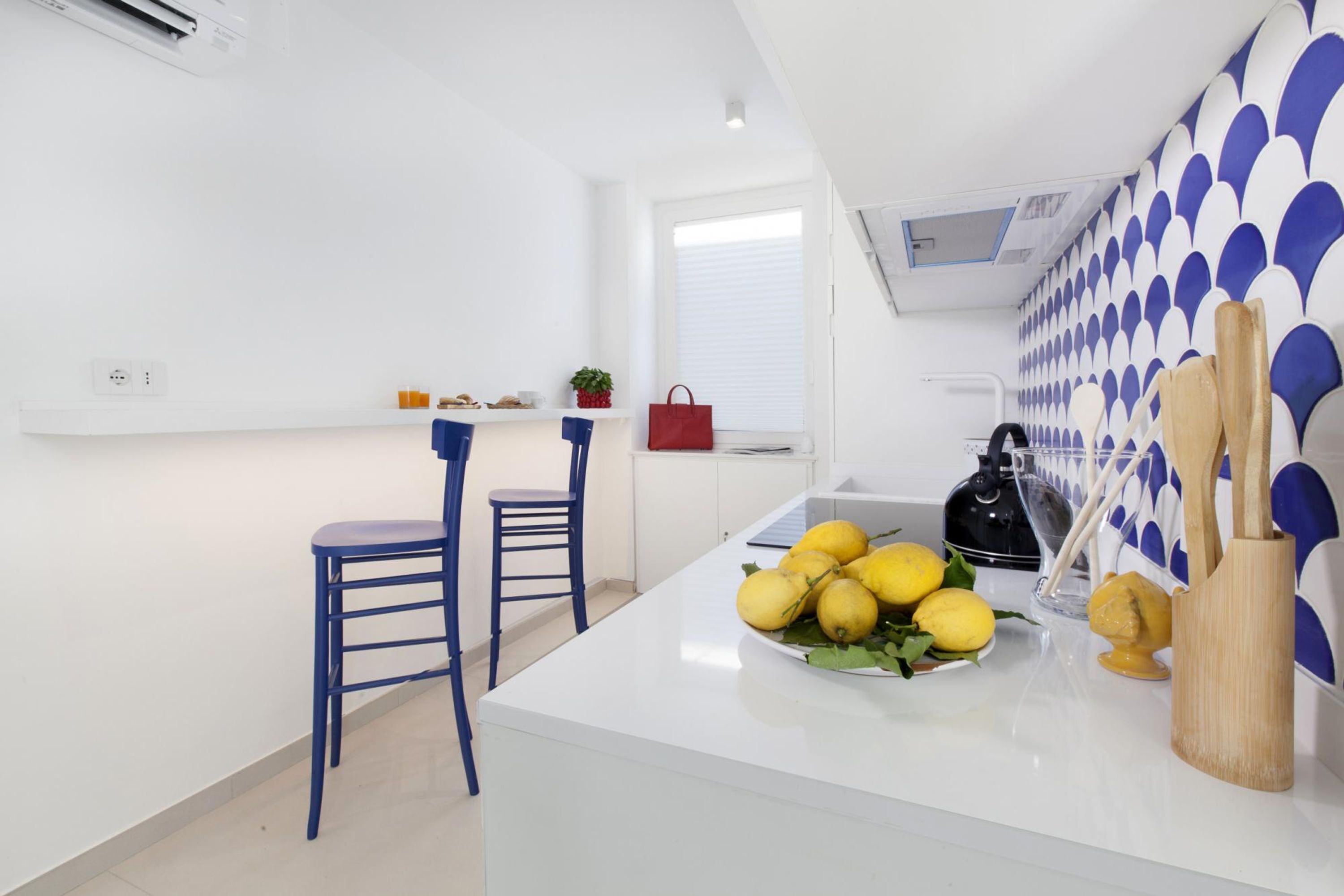 A modern kitchen with a white countertop, two blue chairs, and a bowl of lemons.