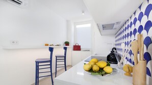 Een moderne keuken met een wit aanrecht, twee blauwe stoelen en een kom met citroenen.