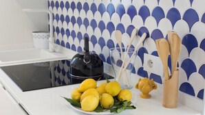 Een keuken met een wit aanrecht, een zwarte waterkoker, een glas met houten keukengerei en een bord met citroenen.