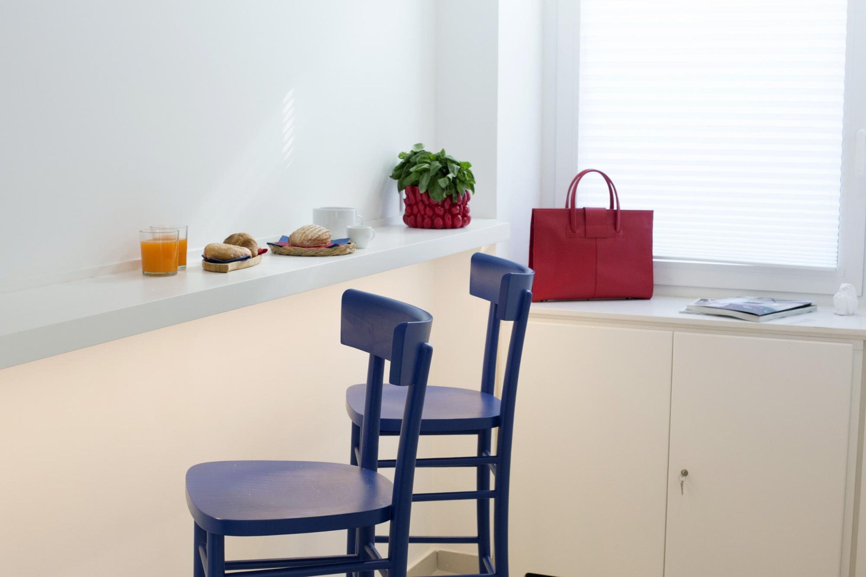 A kitchen area with a white countertop, two blue chairs, a red bag, and a window with blinds.