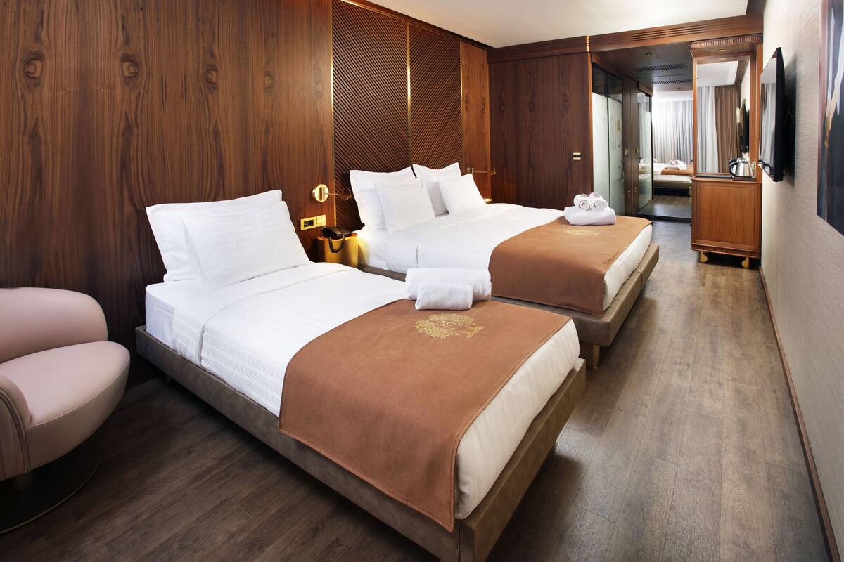 A hotel room with two beds, wooden walls, a wooden floor, a TV, and a bathroom visible through an open door.