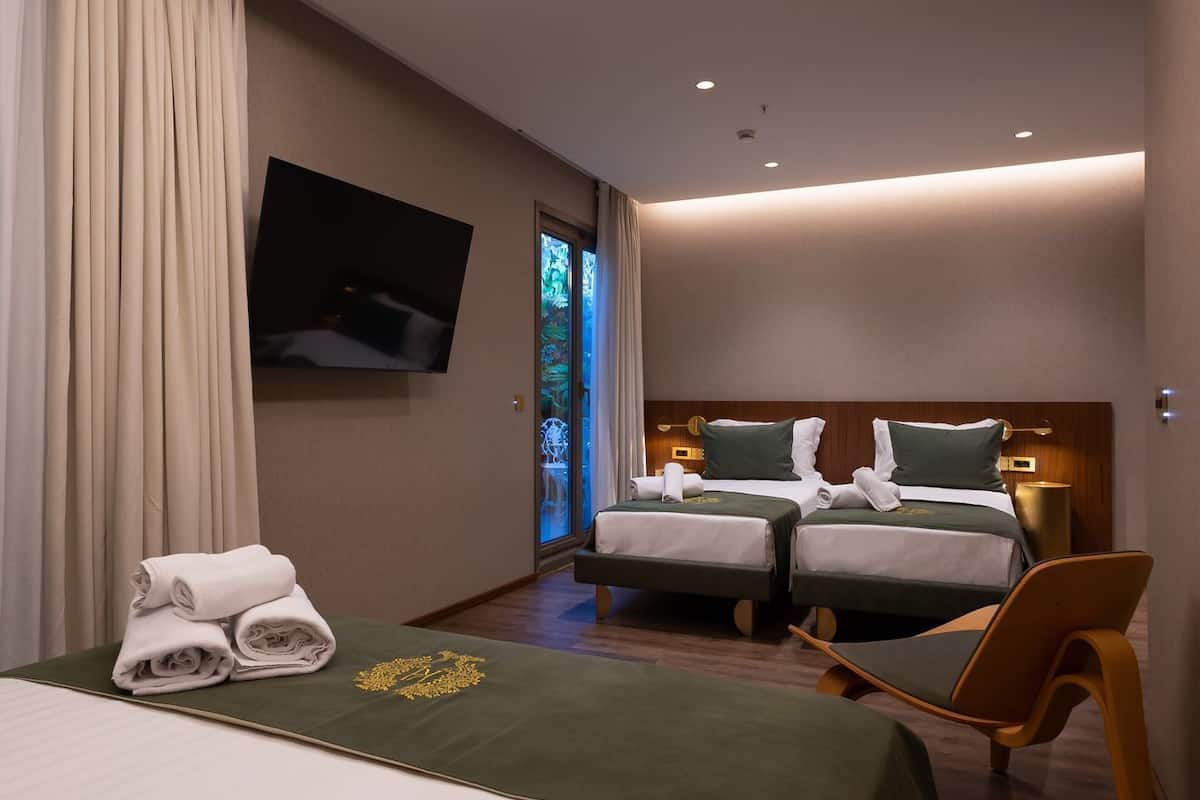 A modern hotel room with a large bed, two smaller beds, a flat-screen TV, and a ceiling light fixture.