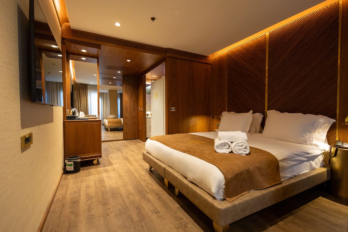 A spacious hotel room with a large bed, wooden paneling, a mirror, and a wooden floor.
