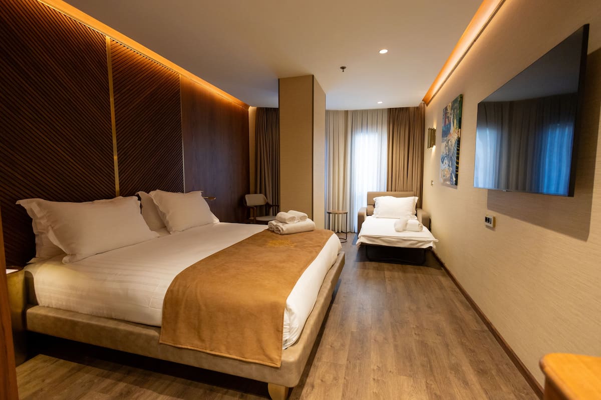 A hotel room with a large bed, a smaller bed, a sofa, and a large mirror.