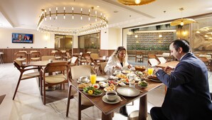 A dining area with wooden tables and chairs, a large chandelier, and a television screen on the wall. - Kate Hotel Special Class & Spa (Istanbul)