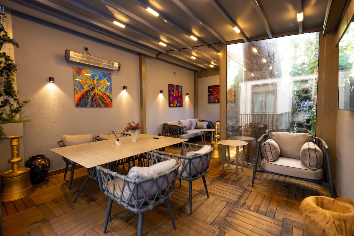 A modern dining area with a wooden herringbone floor, a long table, and wicker chairs. There are wall-mounted lights and artwork above the table.