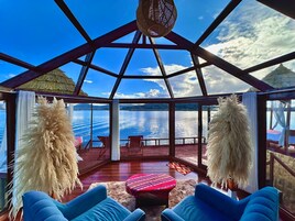 Una habitación con vistas a un lago, techo de madera y una mesa con sillas.