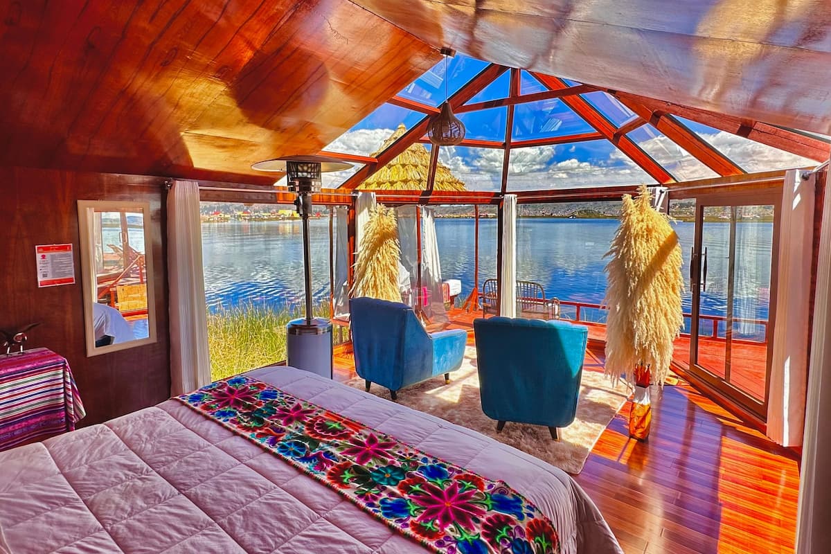 A room with a bed, two chairs, a table, and a large window overlooking a body of water.