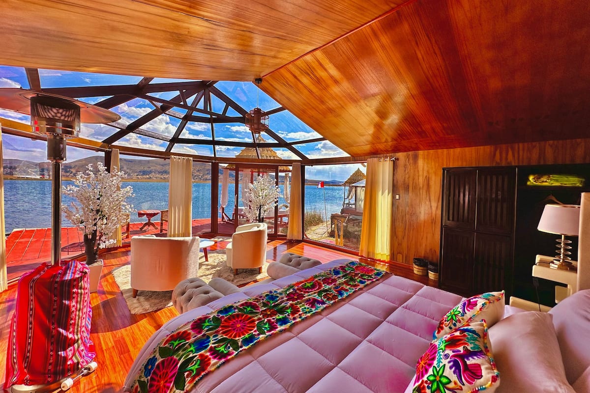 A spacious room with a large bed, a wooden ceiling, and a view of the water outside.